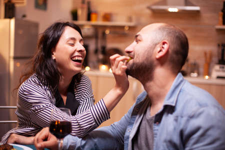 Husband feeding wife with grapes during romantic dinner celebrating relationship. Wife and husband...