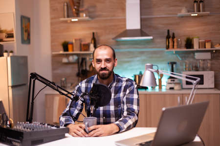 Influencer holding coffee cup and recording podcast in home studio. Creative online show On-air production internet broadcast host streaming live content, recording digital social media communicationの写真素材