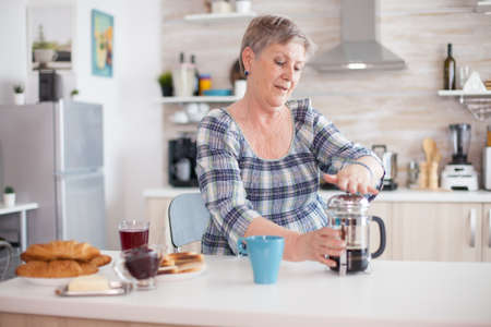 Senior woman enjoying a mug of coffee from french press during breakfast. Elderly person in the morning enjoying fresh brown cafe espresso cup caffeine from vintage mug, filter relax refreshmentの写真素材
