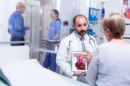 Doctor discussing about heart attack with senior woman because of her medical condition in hospital room. Medical services medicine healthcare well-being support, physician workingの写真素材