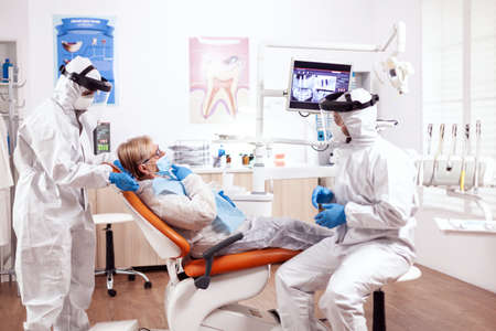 Dentist wearing equipment agasint coronavirus dicussing about teeth hygiene with senior patient....