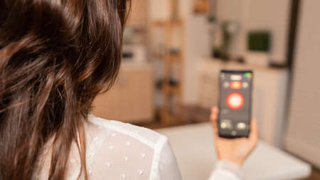 Using smartphone with technology to control home lighting system. Person in apartment holding...
