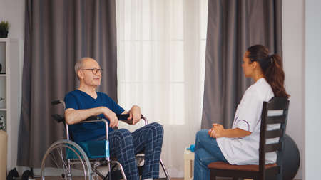 Old man in wheelchair talking with doctor. Disabled disability old person with medical worker in nursing care home assistance, healthcare and medicine serviceの写真素材