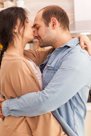 Wife kissing husband nose while dancing in kitchen. Happy young family. Wife and husband love,...