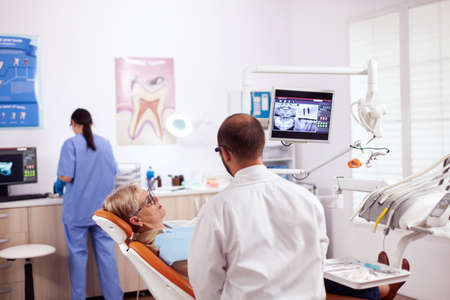 Senior woman discussing with dentist in dental cabinet about teeth issue sitting on chair. Medical...