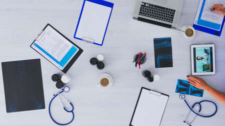 Top view of resident physician discussing with doctor on videocall using tablet, checking appointments on clipboard. Talking with specialist on videomeeting online conference on copy space, flat layの写真素材