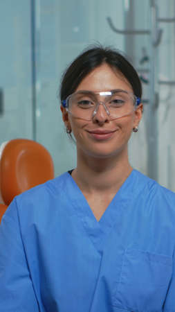 Portrait of smiling nurse in dental office while doctor is talking with patient in background....