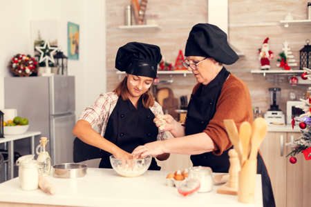 Grandmother wearing apron on christmas day making cookies with niece. Happy cheerful joyfull teenage girl helping senior woman preparing sweets to celebrate winter holidays.の写真素材