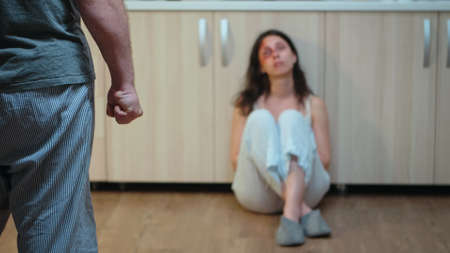 Brutal man clenching fist sitting in front of abused woman. Violent aggressive husband abusing...
