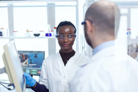 African scientist discussing virus trial with virolog in chemistry laboratory. Multiethnic team of medical researchers working together in sterile lab wearing protection glasses and gloves.の写真素材