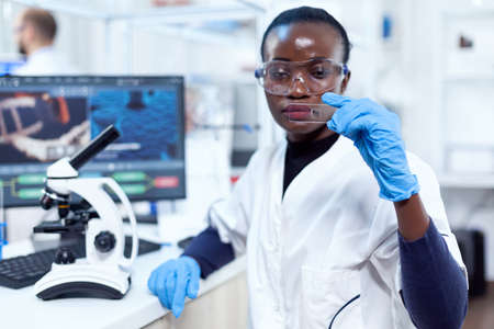 Concentrated view of doctor african scientist holding glass microscope glass. Black healthcare scientist in biochemistry laboratory wearing sterile equipment.の写真素材