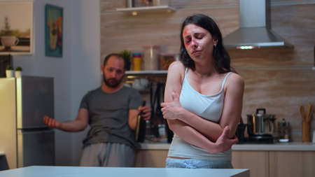 Beaten woman trembling of pain and fear. Traumatised abused terrified assaulted wife covered in bruises suffering injury from alcoholic aggression brutal violent man.の写真素材