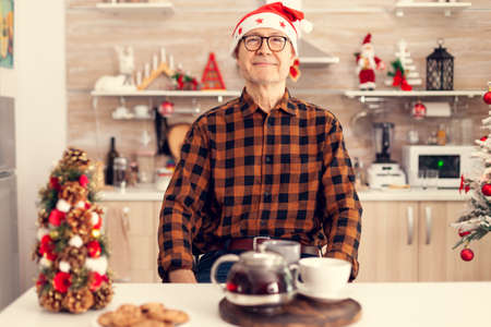Happy old man with gray hair celebrating christmas wearing santa hat enjoying delicious cookies....