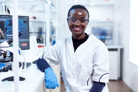 Portrait of professional african scientist smiling at camera in sterile laboratory. Multiethnic team...