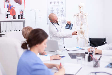 Doctor explaining radiography in front of his medical staff in hospital conference room. Clinic...