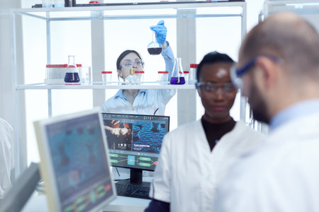 Scientist picks up glass flask with colored liquid in laboratory. Multiethnic team of medical...