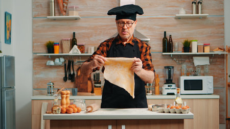 Chef cooking handmade pasta with healthy ingredients at home in modern kitchen. Happy elderly baker...