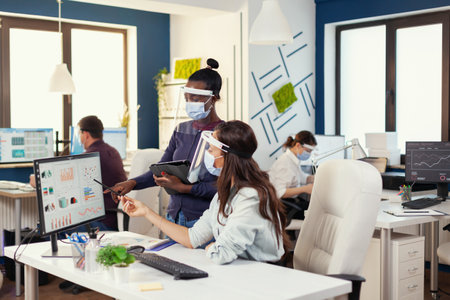 African manager giving indication to employee at workplace wearing face mask agasint covid19. Diverse team working respecting social distancing during global pandemic with coronavirus. New normal.の写真素材
