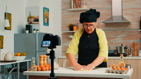 Old baker recording culinary video in kitchen preparing homemade pizza. Retired blogger chef...