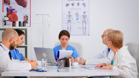 Group of doctors with laptop computer and clipboard with documents meeting and discussing at medical office. Nurse presenting symptoms of disease, colleagues taking notes during brainstorming.の写真素材