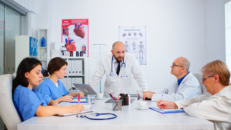 Medical team listening specialist doctor and taking notes during brainstorming sitting in hospital meeting room. Surgeon explaining treatment to coworkers presenting plan during medical conferenceの写真素材