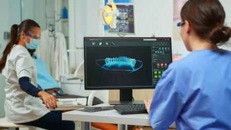 Dentist assistant writing parameters from digital dental fingerprint of patient, while specialist...