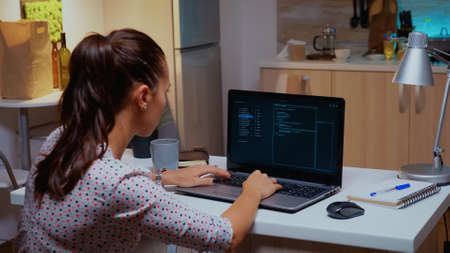 Back view of woman hacker coding a dangerous virus to attack company database in midnight....