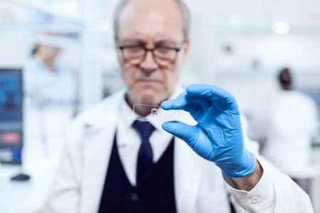 Close up of medicine sample on glass slide while scientist is looking at it in laboratory. Senior...