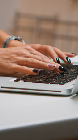 Close up of woman typing on laptop sitting in the kitchen late at night and working. Busy focused employee using modern technology network wireless doing overtime for job reading writing, searchingの写真素材
