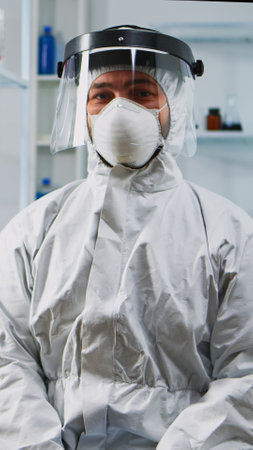 Portrait of experienced scientist man in coverall smiling at camera wearing protection mask in equipped lab. Examining virus evolution using high tech and chemistry tools for vaccine development.の写真素材