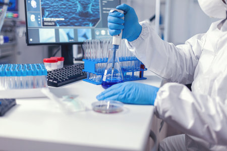 Medic in protective suit conducting test for coronavirus using automatic pipette. Chemist in modern laboratory doing research using dispenser during global epidemic with covid-19.の写真素材