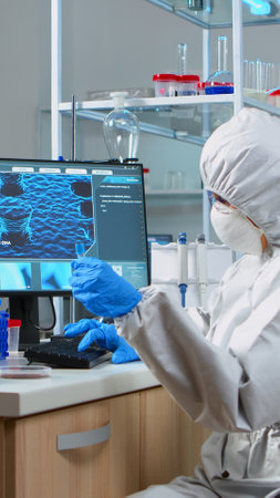 Chemist with coverall looking at virus test in equipped lab. Scientist working with various...