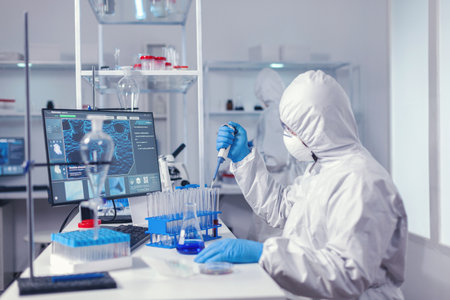 Engineer in microbiology lab holding micropipette with sample from test tube. Chemist in modern laboratory doing research using dispenser during global epidemic with covid-19.の写真素材