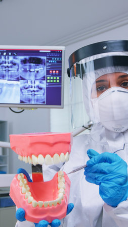 Patient pov of dentist showing correct way of cleaning teeth wearing precaution against covid in dental office using skeleton accessory. Stomatolog wearing safety gear during heatlhcare checkの写真素材