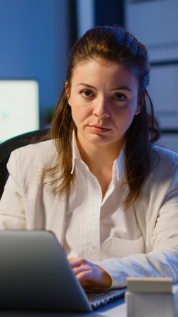 Tired woman manager raising head looking at camera sighing after typing on laptop, working late at night in start-up business office. Focused employee using technology network wireless doing overtimeの写真素材
