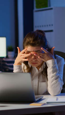 Stressed businesswoman suffering from headache at work doing overtime late night. Exhausted tensed worker coping with migraine, emotional stress concept feeling pain sitting at office desk with laptopの写真素材
