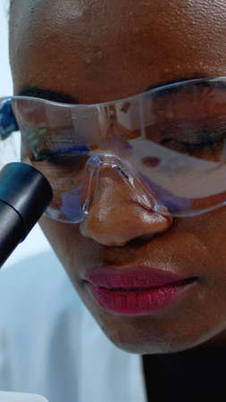 Close up of african woman doctor analysing virus using microscope. Multiethnic team examining...