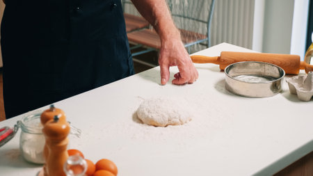 Close up of retired baker pouring wheat flour on dough for bread. Elderly senior baker with bonete...