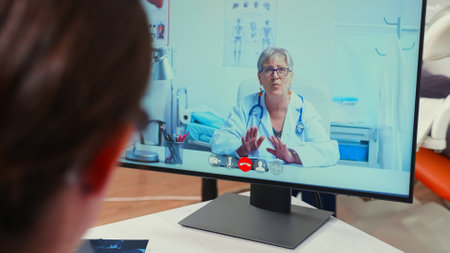 Back view of nurse discussing on webcam with senior specialist stomatologist using mobile phone...