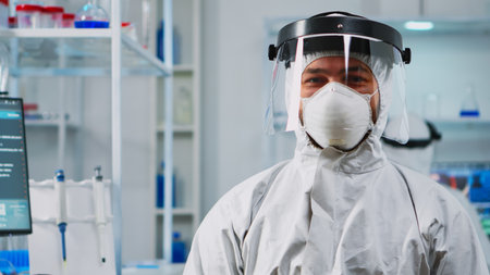 Portrait of scientist man wearing coverall smiling at camera sitting in modern equipped laboratory....