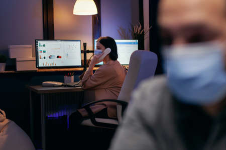 Businesswoman with medical mask standing at office talking on phone. Stressed man in corporation...