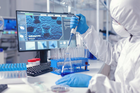 Micropipette used by medical researcher in laborator in time of virus dressed in protection suit. Chemist in modern laboratory doing research using dispenser during global epidemicの写真素材