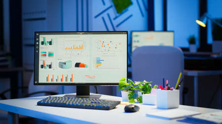Interior of empty start up business office with modern design during night with graphics running on the desktop. Financial company with nobody in it, place of work startup, workplace indoors conceptの写真素材