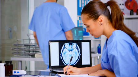 Radiologist analysing radiography film and writing diagnosis on clipboard in hospital clinic,...