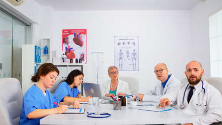 Team of doctors discussing online with chief phisycian, training medical workers group, teaching medic team in virtual conference web camera. Medic having video conference sitting in hospital officeの写真素材