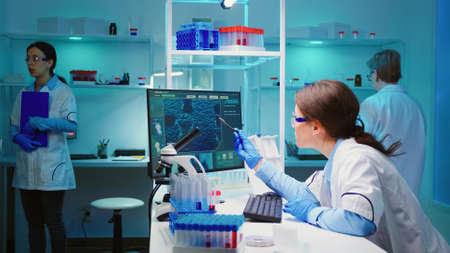 Woman biochemist checking manifestations of virus working on computer in equipped lab late at night....