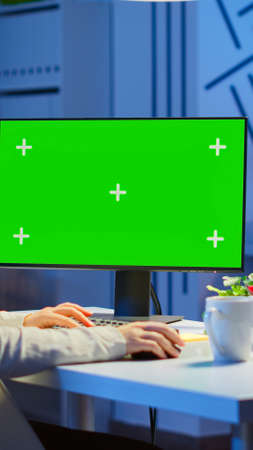 Businesswoman looking at green screen monitor of computer sitting at desk in business office late at...
