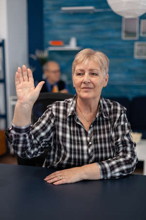 Thoughtfull elderly lady greeting people in the course of online conference. Happy senior woman with...