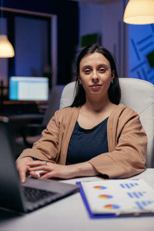 Portrait of hard working manager looking into camera doing overtime. Smart woman sitting at her...