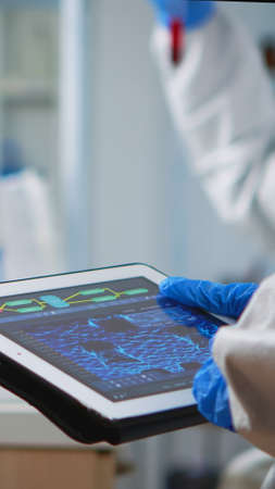 Back view of scientist in coverall analyzing virus evolution looking on digital tablet. Team of microbiologists conducting vaccine development using high tech for researching treatment against covid19の写真素材